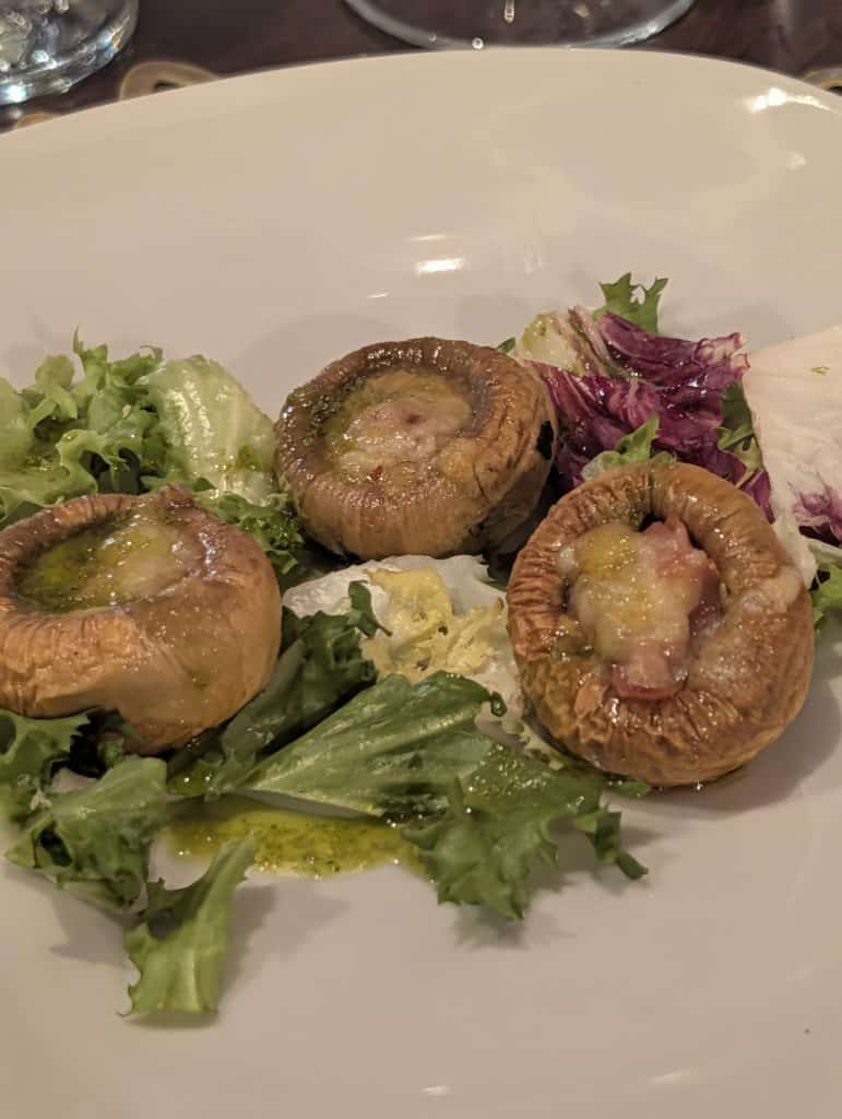 Picture of a plate of gratinéed mushrooms with jamón ibérico laid over the top
